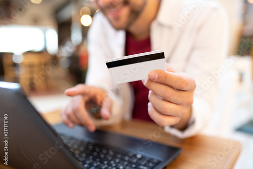 A man in a cafe with a laptop and a credit card, focus on the credit card.