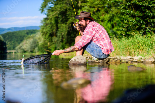 successful fisherman in lake water. big game fishing. relax on nature. hipster fishing with spoon-bait. mature bearded man with fish on rod. fly fish hobby. Summer activity. What a fish