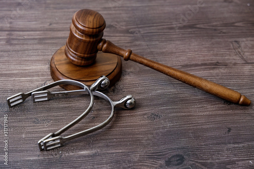 Concept for horse auction or trial. Wooden gavel and pair of spurs on wooden table.