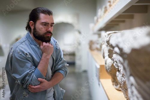 Man visiting sculpture hall in historical museum and looking at exhibits