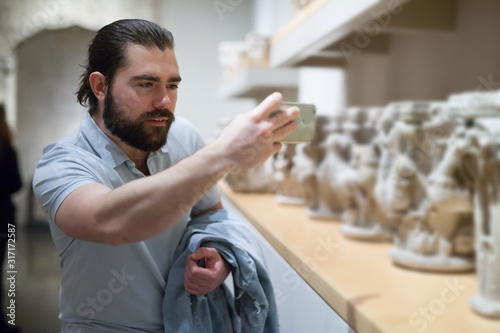 Adult male visitor using phone in sculptures exposition at museum