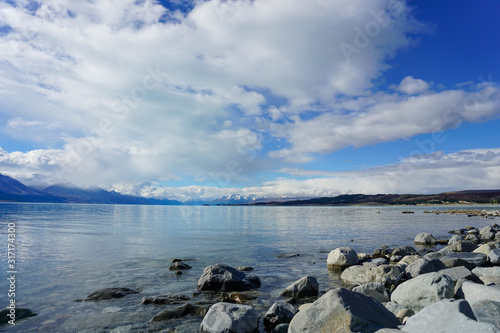 The sandy beach by the lake, behind the mountains, there are rocks and the sky.