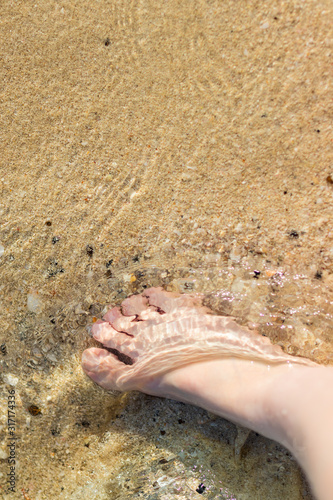 bare foot of a woman in the clean and transparent sea water with yellow sand and sea stones.