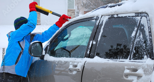 Female clearing winter snow from her car outside.