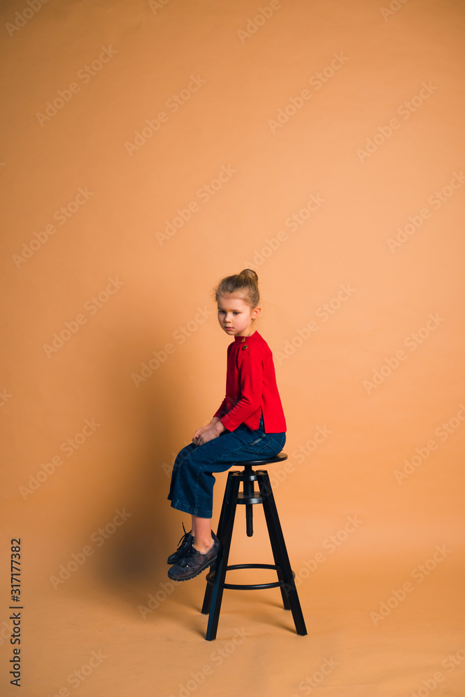young girl wearing trendy fashion outfit sitting on high stool in studio with color background young girl wearing trendy fashion outfit sitting on high stool in studio with color background