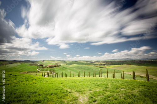 Collina Toscana, con laghetto in primo piano e filari di cipressi sul bordo di una strada sterrata che porta ad un casa immerso nelle verdi colline © gio_cala