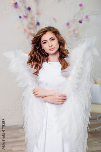 Portrait of a young girl, an angel in a white dress stands wrapped in wings.