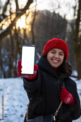 young smiling woman in winter outfit holding phone with white blank empty screen
