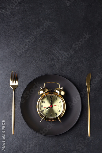 Interval fasting concept with a golden alarm clock on a black plate