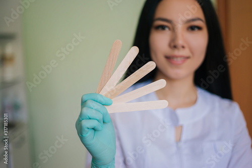 The girl in a white coat holding wooden sticks for depilation.