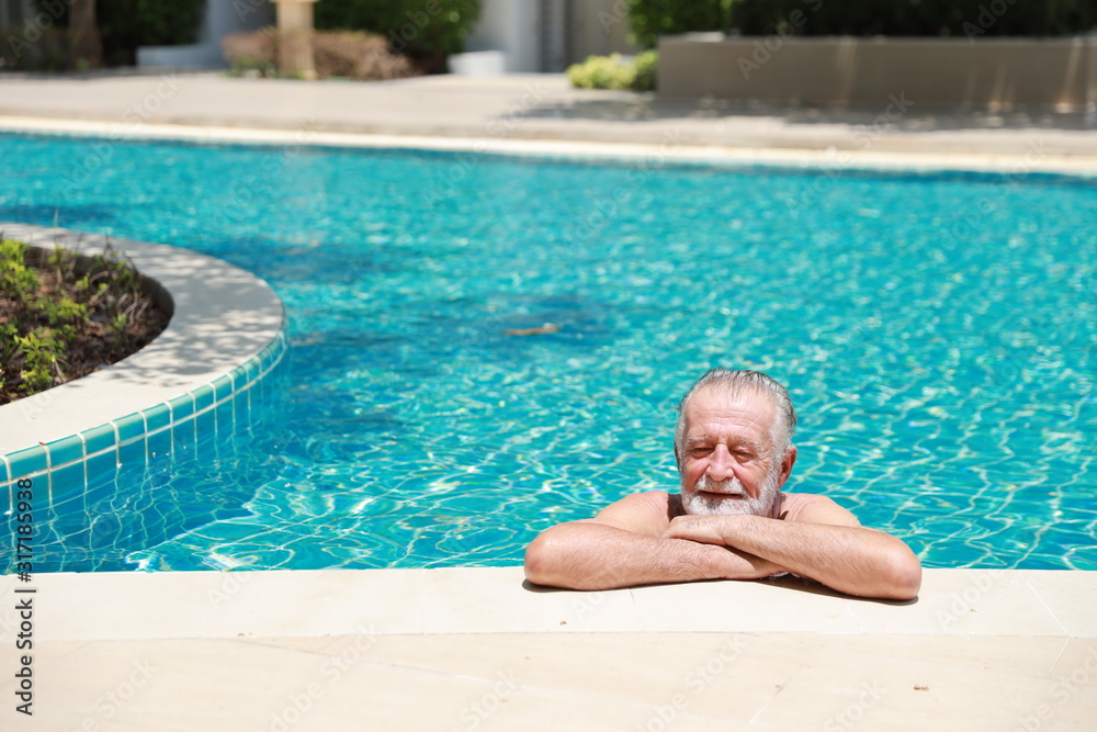 Happy elderly caucasian swimming in pool during retirement holiday with relaxation and smiling. Old man having good time in hotel outdoor with happy face
