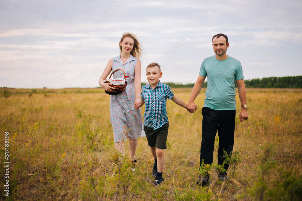 The boy leads the hands of his parents. Happy family in the fresh air. A family of three walking around the field
