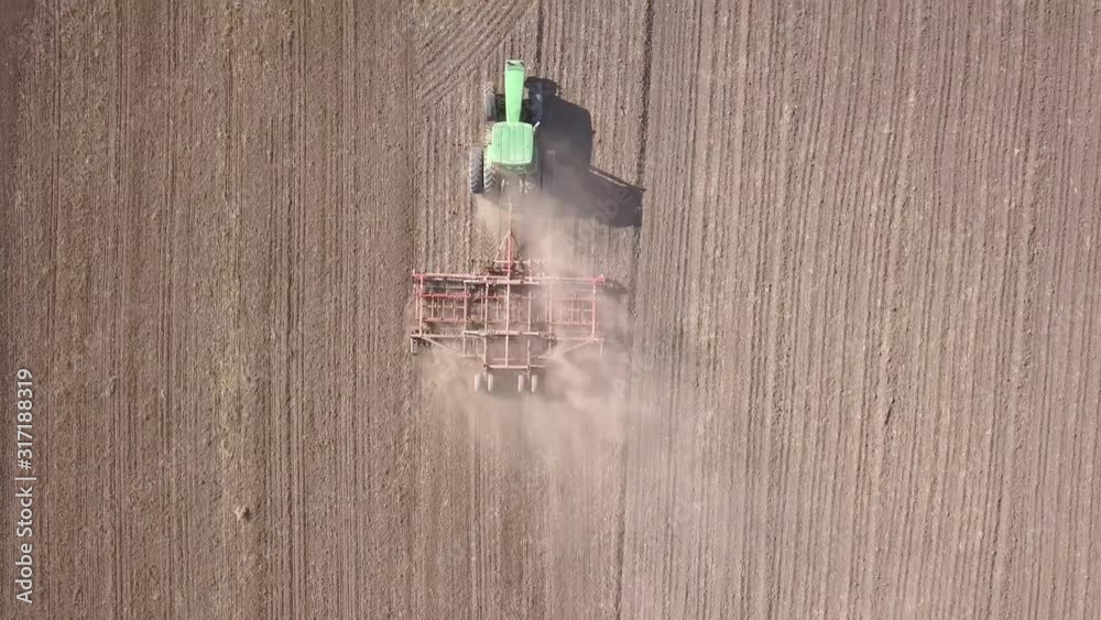 Top down aerial view of green tractor cultivating ground and seeding a dry field. Farmer preparing land with seedbed cultivator as part of pre seeding activities in early spring season. Top down aerial view of green tractor cultivating ground and seeding a dry field. Farmer preparing land with seedbed cultivator as part of pre seeding activities in early spring season.