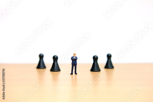 Business strategy conceptual photo - Miniature of businessman standing in the middle on chess pawn at wooden table