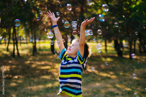 A boy in a striped T-shirt catches soap bubbles. The child plays on a walk.