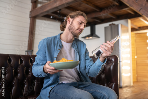 Man drinking beer and eating chips while staying at home