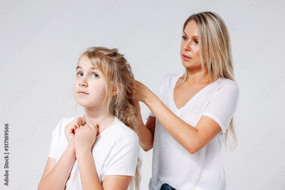 Young beautiful blonde woman make hair style for girl. Joint leisure of mother and daughter. Isolated on white background Young beautiful blonde woman make hair style for girl. Joint leisure of mother and daughter. Isolated on white background