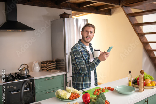 Smiling man texting with his friend while cooking