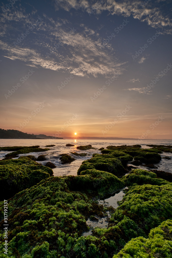 Sunrise over a beach with coral reefs covered by green moss in Sawarna, Banten, Indonesia
