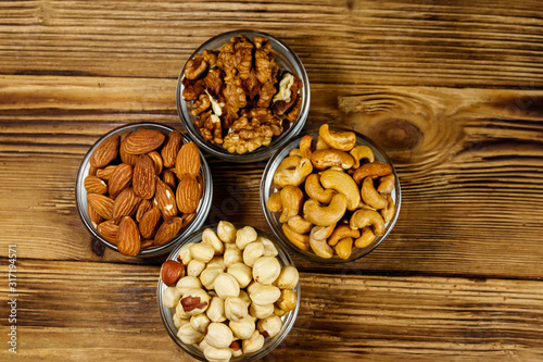 Assortment of nuts on wooden table. Almond, hazelnut, walnut and cashew in glass bowls. Top view. Healthy eating concept