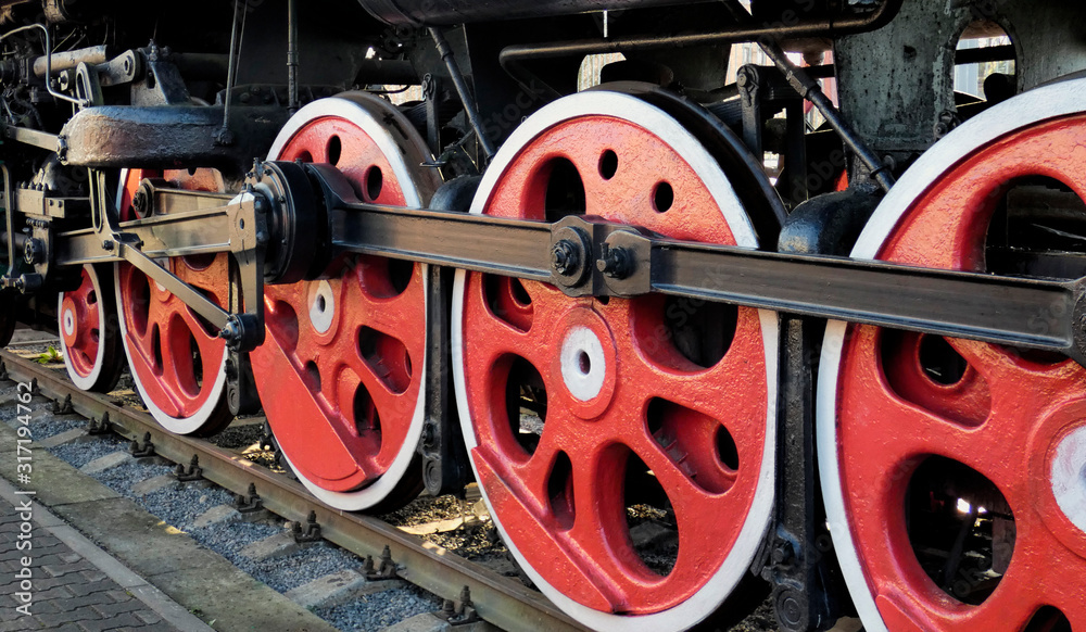 Old steam engine locomotive wheels and other parts, close-up view. Black and red iron details of vintage train. Industrial retro background.