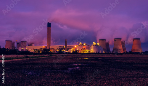 Drax, North Yorkshire, UK  on a cold winter's night. The bright lights of a power station are reflected in  a waterlogged farmer's field. Plumes of water vapour from the cooling towers fill the sky