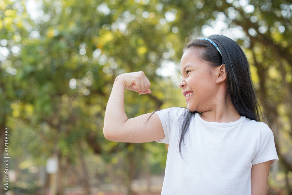 happy Little asian girl child standing showing front teeth with big smile. showing arms muscles smiling proud. Looking camera showing biceps. fresh healthy green bio background. Fitness concept. happy Little asian girl child standing showing front teeth with big smile. showing arms muscles smiling proud. Looking camera showing biceps. fresh healthy green bio background. Fitness concept.