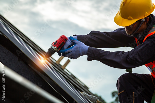 Valokuva [Construction roof] Roofer worker in protective uniform wear and gloves, Construction worker install new roof,Roofing tools,Electric drill used on new roofs with Metal Sheet