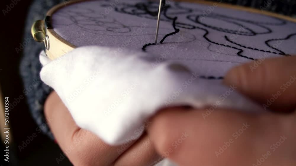 Mano femenina bordando textura abstracta sobre tela blanca