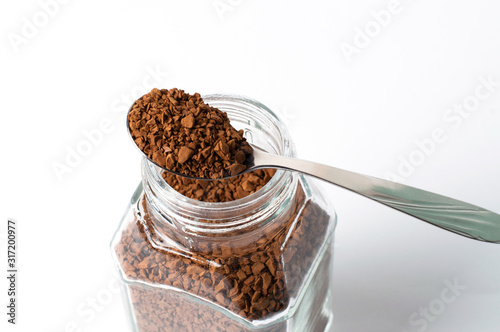 Instant coffee in spoon and a jar on a white background, granules closeup photo