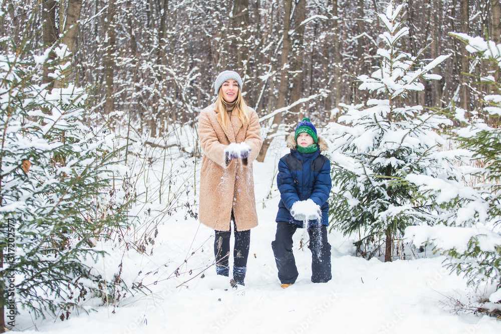 Parenting, fun and season concept - Happy mother and son having fun and playing with snow in winter forest
