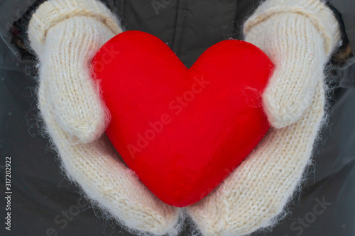 Female hands in white fluffy mittens hold a red heart. Valentine s day concept. A symbol of love  devotion and happiness. Festive winter card.