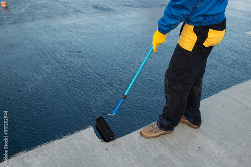 Fotografija Worker applies bitumen mastic on the foundation