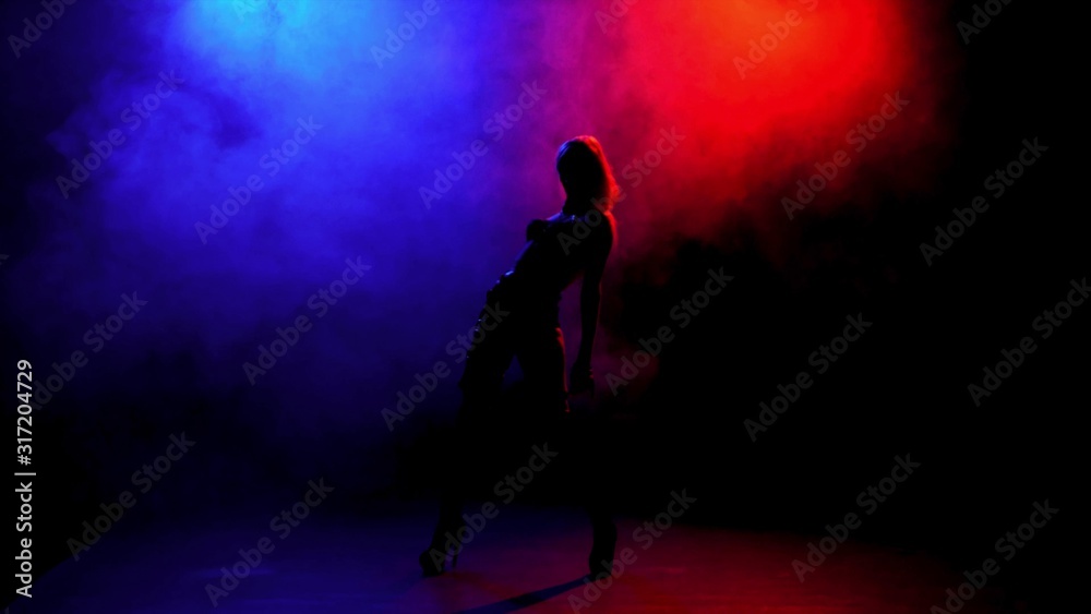 Silhouetted girl dancing in the dark on a background of smoke smoke red and blue