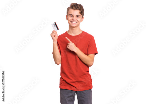 Portrait of happy teen boy with credit card, isolated white background. Smiling child pointing finger on card. Teenager showing credit or debit card having fun.