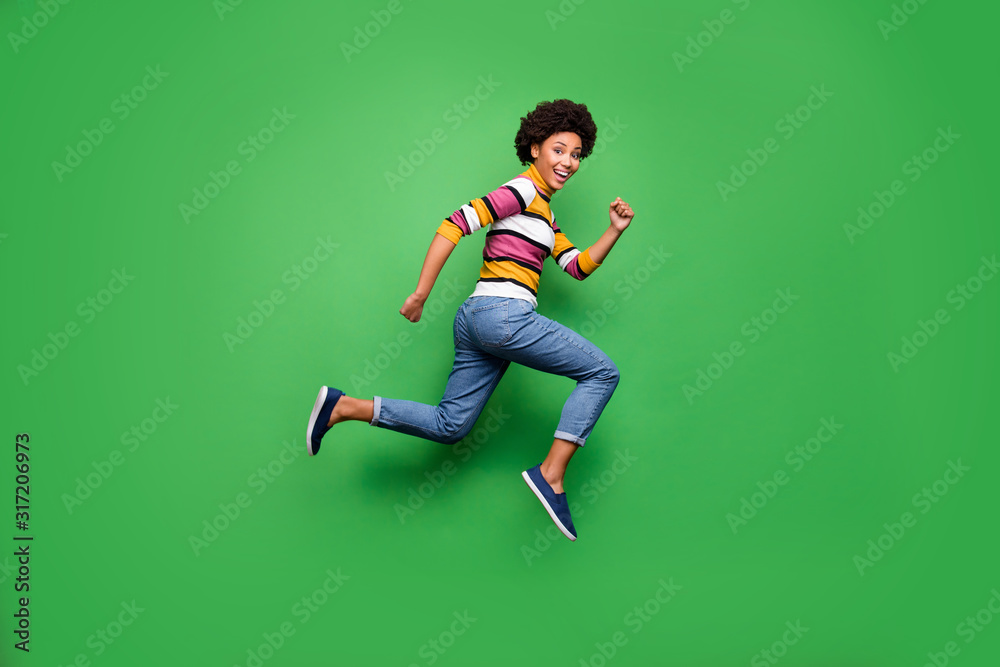 Fotka „Full size profile side photo of positive cheerful afro american girl  jump run after fall black friday bargain wear denim jeans outfit isolated  over green color background“ ze služby Stock