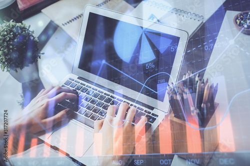 Double exposure of stock graph with businessman typing on computer in office on background. Concept of hard work.