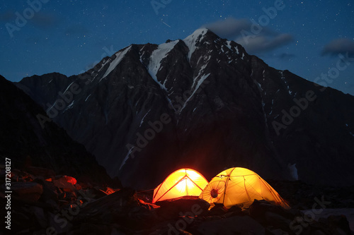 Starry night mountain landscape with glowing tents.