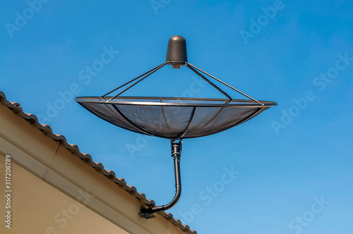 Satellite dish  television antenna on house roof with clear blue sky.