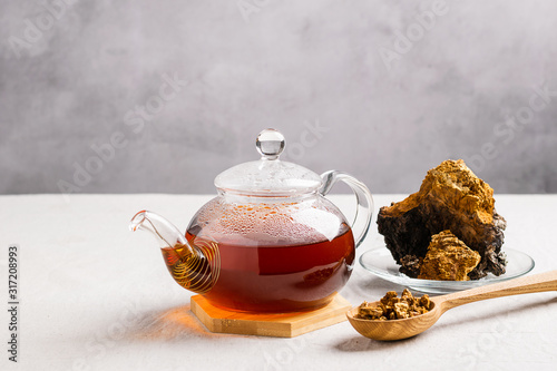 Healing tea from chaga birch mushrooms in a glass teapot. Organic drink antioxidant gray background.