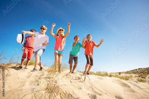 Group of happy kids jump from the sand hill up