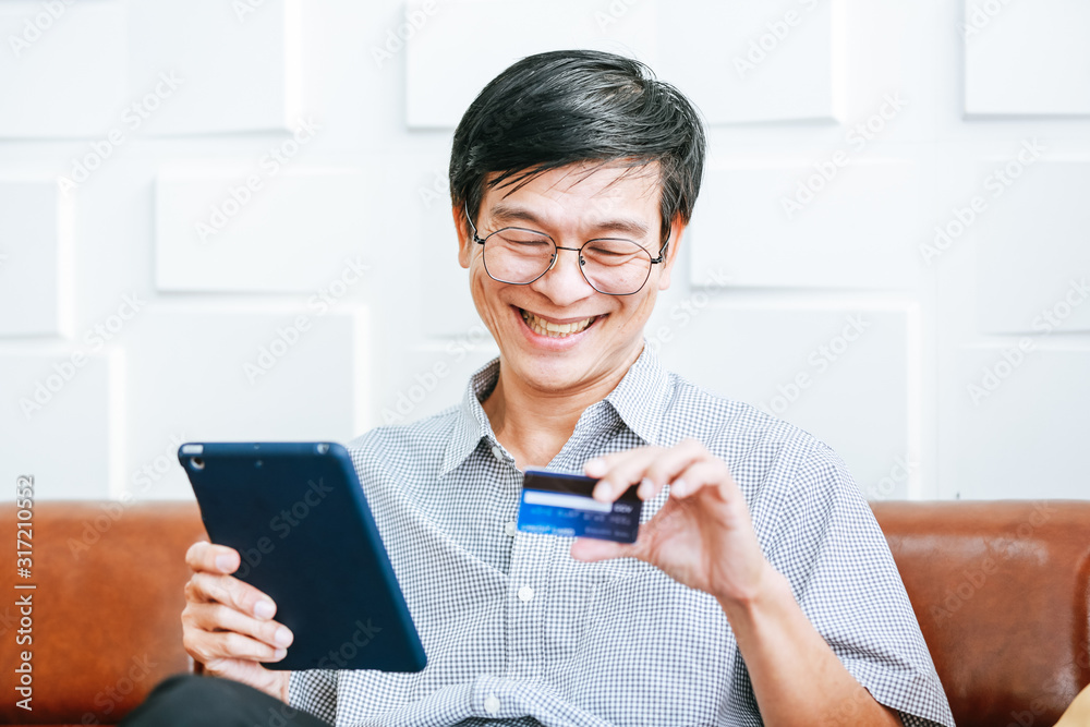 The aged Asian businessman holds a credit card to view online spending. The aged Asian businessman holds a credit card to view online spending.