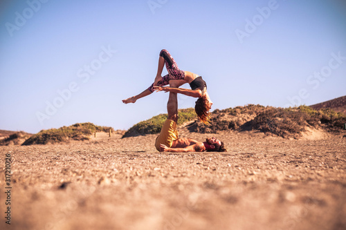 couple of two adults doing acroyoga together at the beach on the sand - man holding his teammate with his legs © Daniel