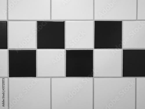 Small square tiles alternately arranged in black and white as a pattern - above and below are larger, square white tiles - separated by joints.