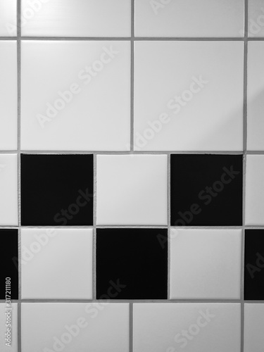 Small square tiles alternately arranged in black and white as a pattern - above and below are larger, square white tiles - separated by joints.
