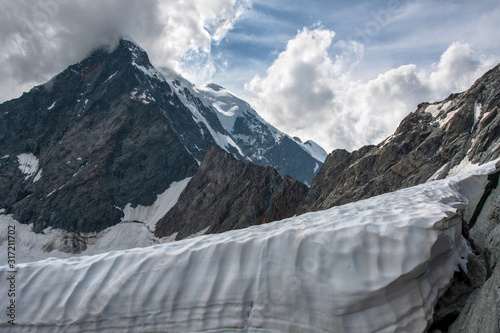 Alpine landscape. View at snow wall of glacier and covered with snow and ice peak.