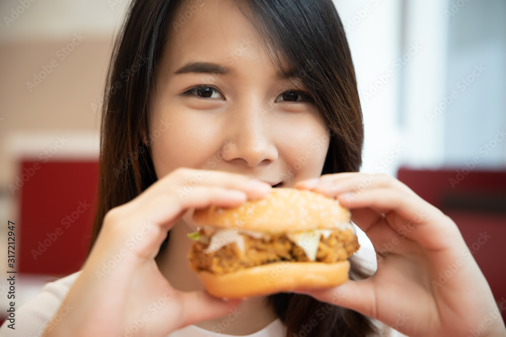 hungry woman looking, eating fried chicken burger; concept of delicious food, junk food, fast food, health care, eating habit, crispy tasty fried chicken burger; asian young adult woman model hungry woman looking, eating fried chicken burger; concept of delicious food, junk food, fast food, health care, eating habit, crispy tasty fried chicken burger; asian young adult woman model