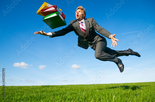 Clumsy businessman tripping dramatically outdoors with his file folders in a green grass meadow