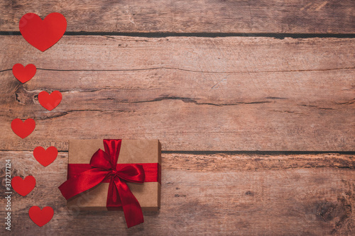 Paper hearts and a craft present with red ribbon on a wooden background. Top side angle view, flat lay. Valentines day concept. Copyspace.