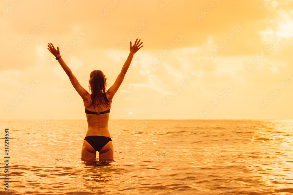 Woman's silhouette with raised arms against calm sunset beach